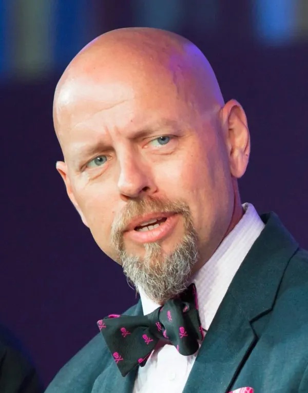 Richard Bird speaking, in a dark suit and a bow tie patterned with pink skulls